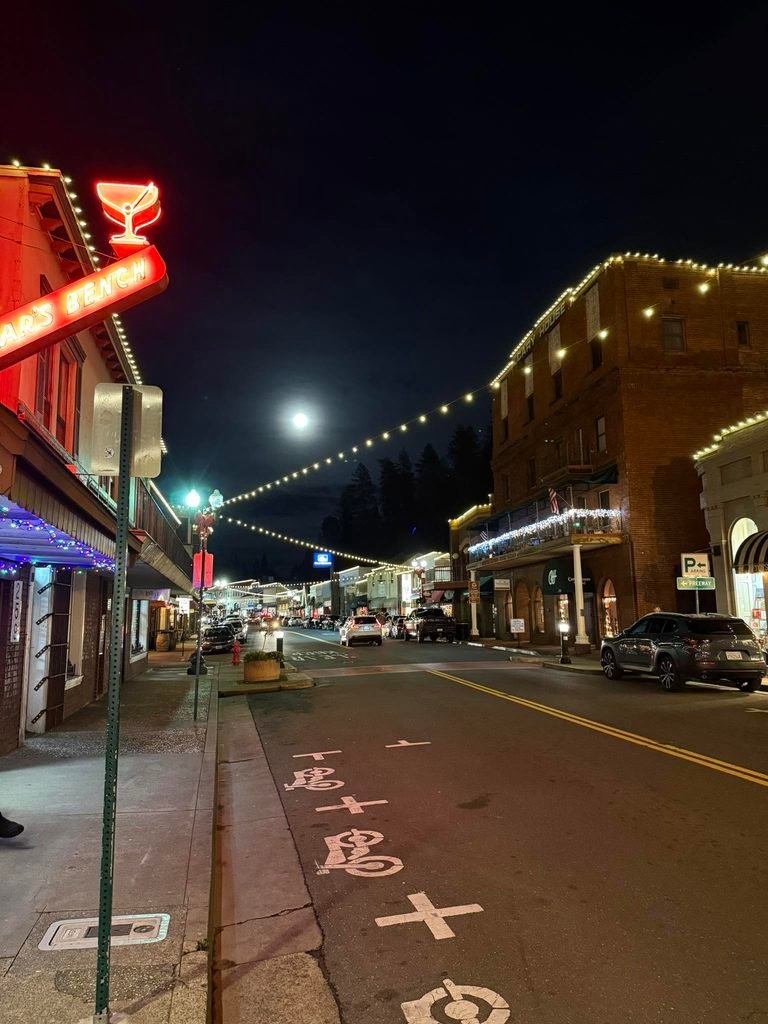 Placerville Main Street at night, with the Cary House Hotel and illuminated storefronts beneath a full moon.